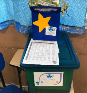 An OHI-Box with a gold star sticker and a lesson chart on a classroom desk