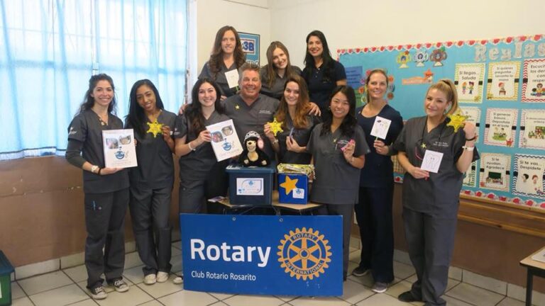 Volunteers holding booklets in a classroom behind a Rotary banner