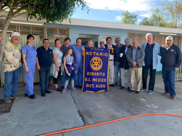 Rotarians standing with a Rotario Rosarito, B.C. Mexico club banner outside a school