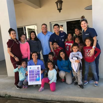 Children and dental volunteers holding a sugar board poster outside a clinic