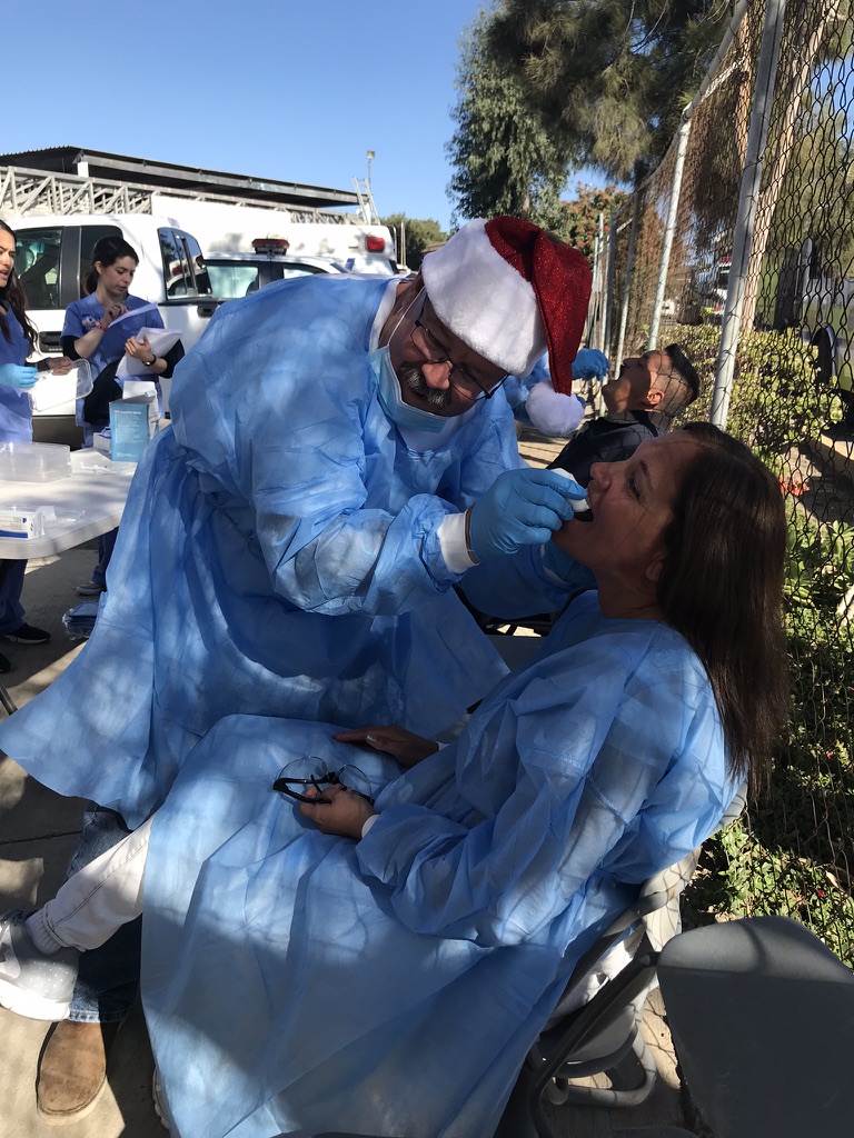 A volunteer dentist in a Santa hat examining a patient at an outdoor screening